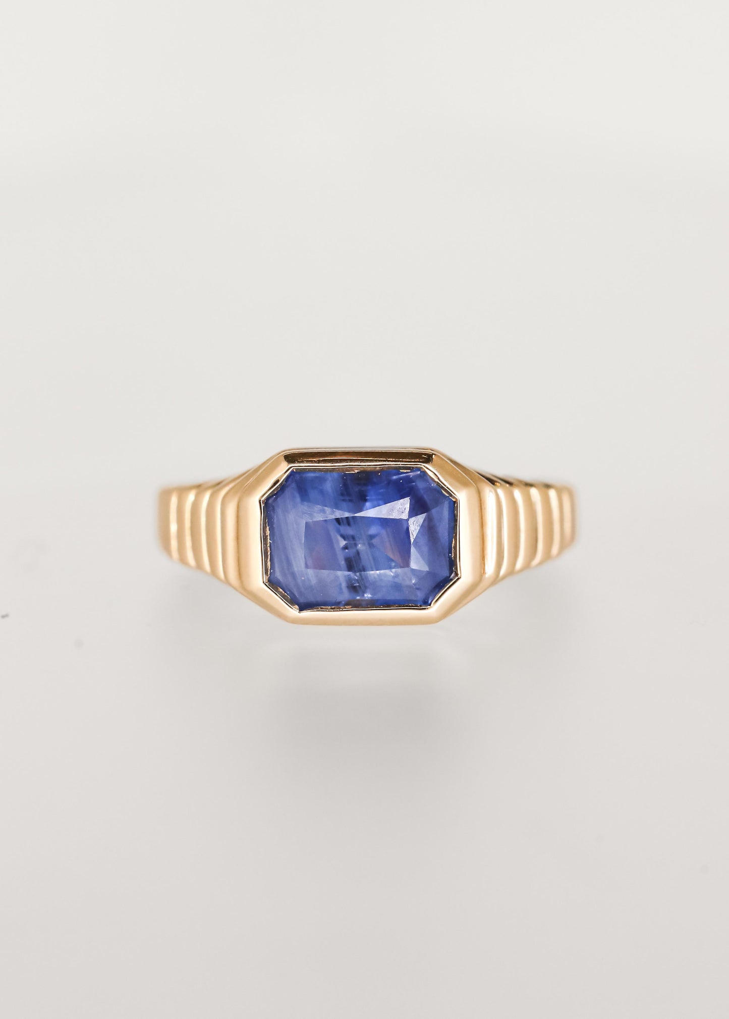 Masculine leaning east west emerald cut blue sapphire engagement ring in 14K yellow gold with a sculptural ribbed signet bezel