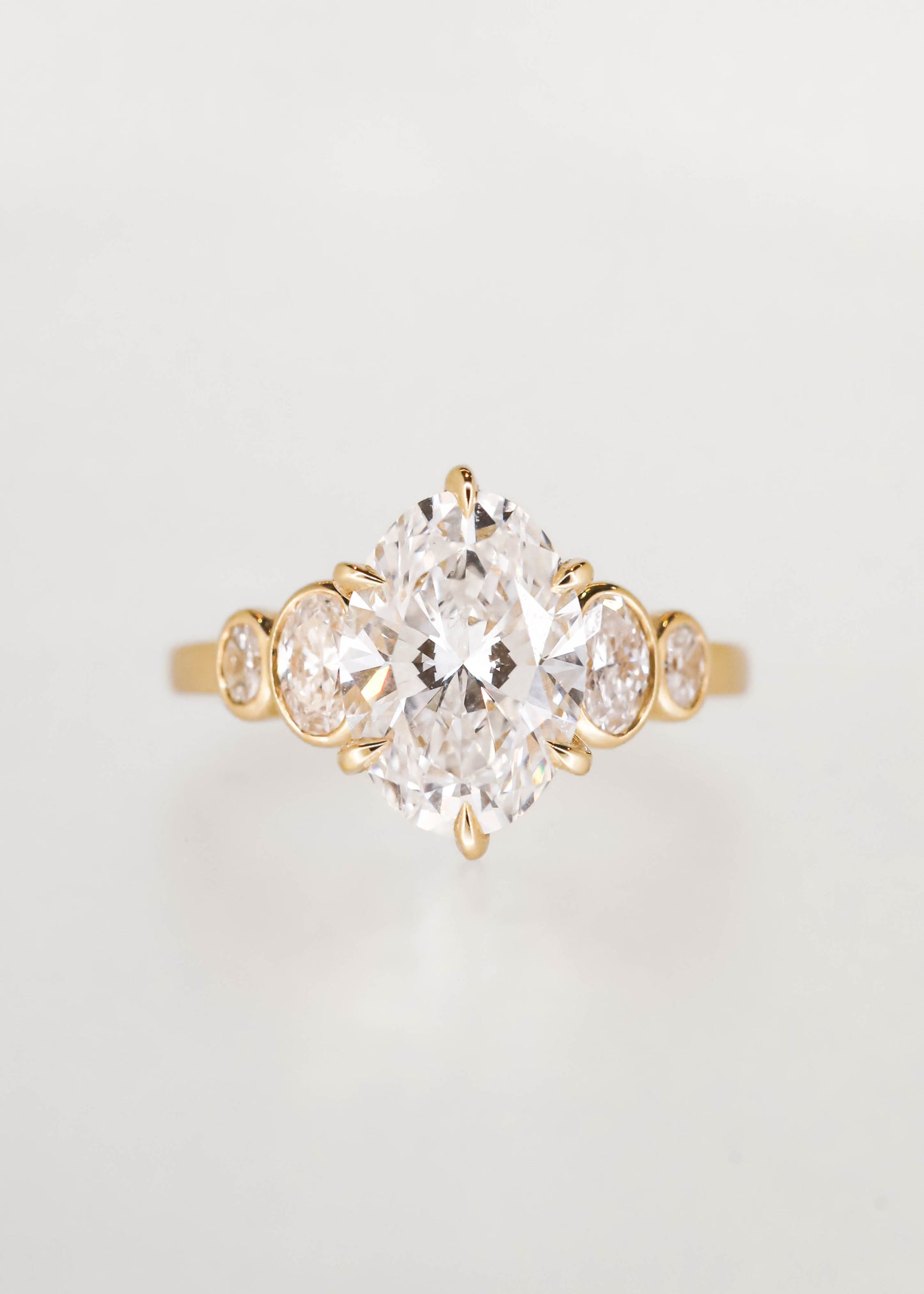Five stone oval cut lab grown diamond engagement ring in 14K yellow gold with a six prong center and graduated bezel side stones
