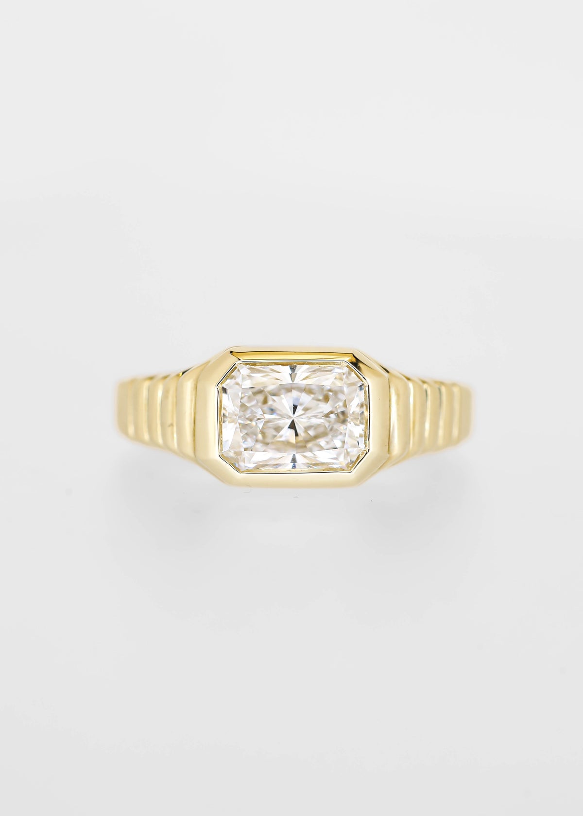 East west bezel set radiant cut lab grown diamond engagement ring in 14K yellow gold with a ribbed band