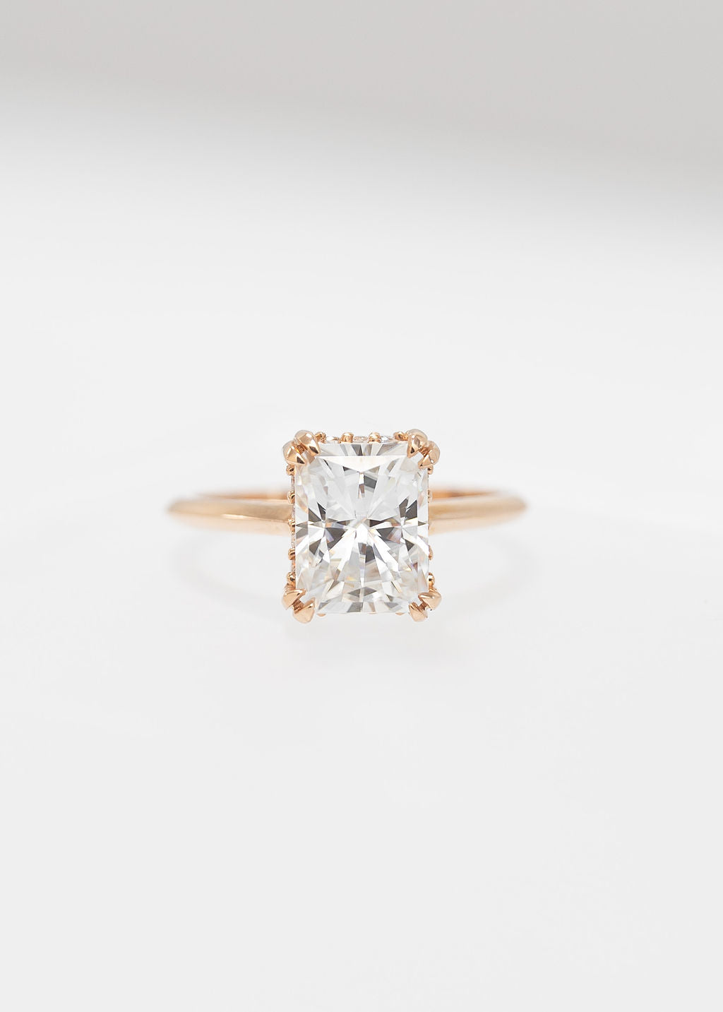 Radiant cut moissanite solitaire engagement ring in 14K rose gold with a double claw basket and hidden halo