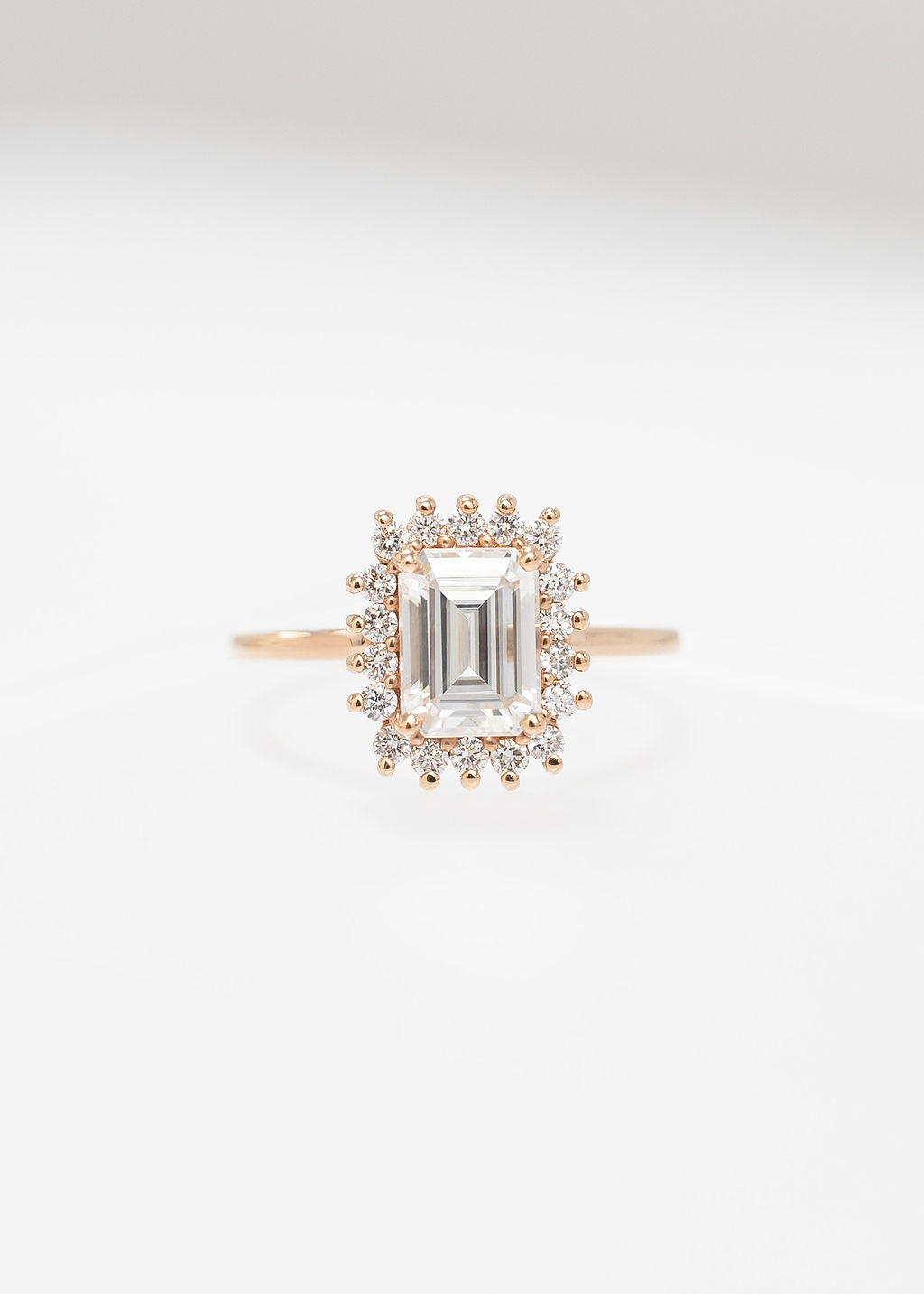 Emerald cut moissanite sunburst halo engagement ring in 14K rose gold with a round diamond halo