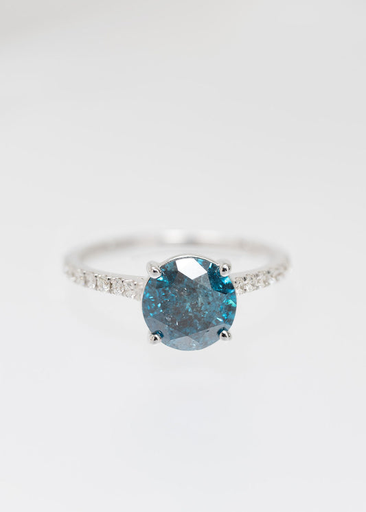 Color enhanced blue diamond solitaire engagement ring in 14K white gold with a pavé band