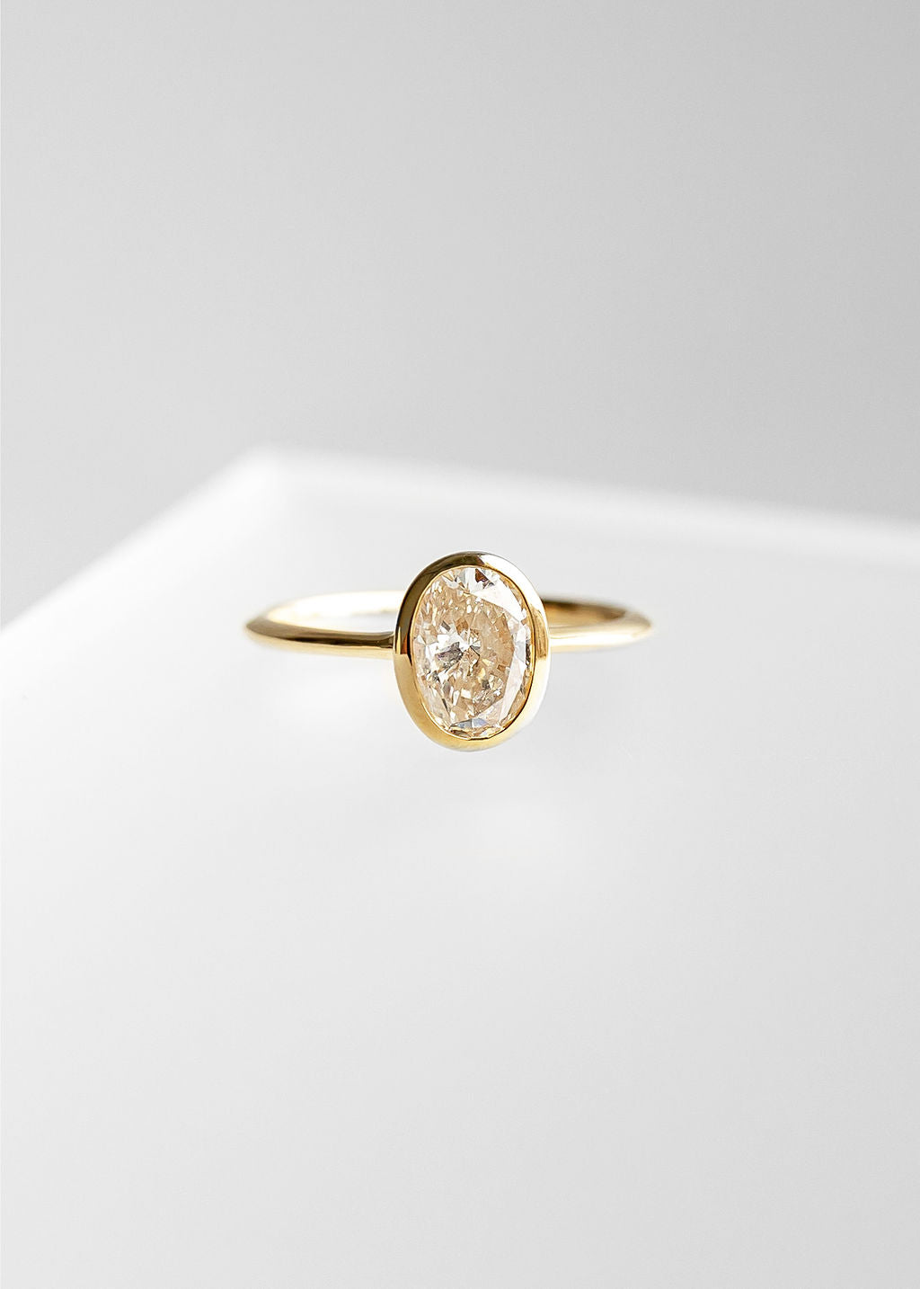 Minimal oval natural diamond bezel solitaire engagement ring in 14K yellow gold with a dainty band and low setting