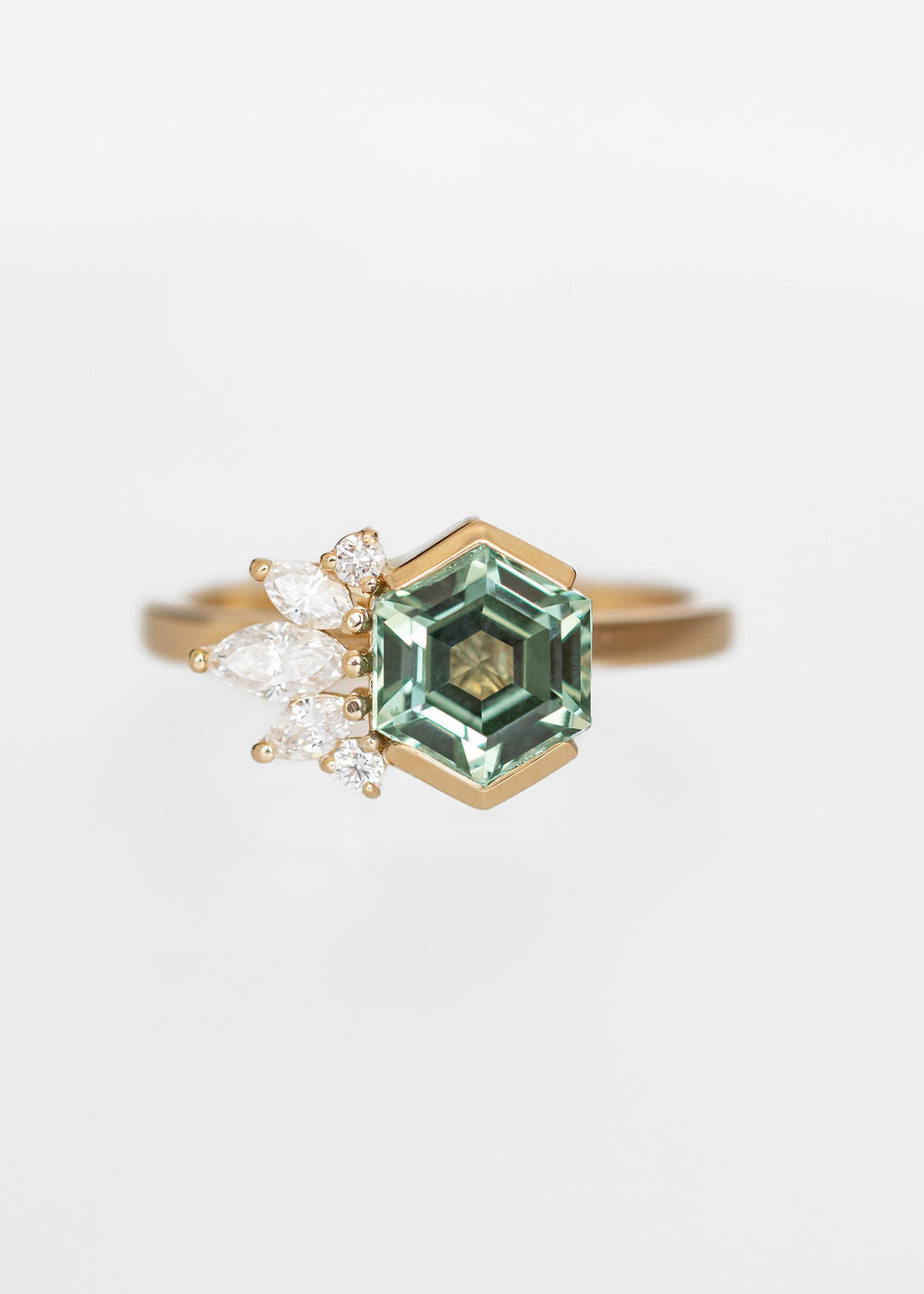 Whimsical hexagon cut green sapphire engagement ring in 14K yellow gold with a half bezel and asymmetrical marquise and round diamond cluster