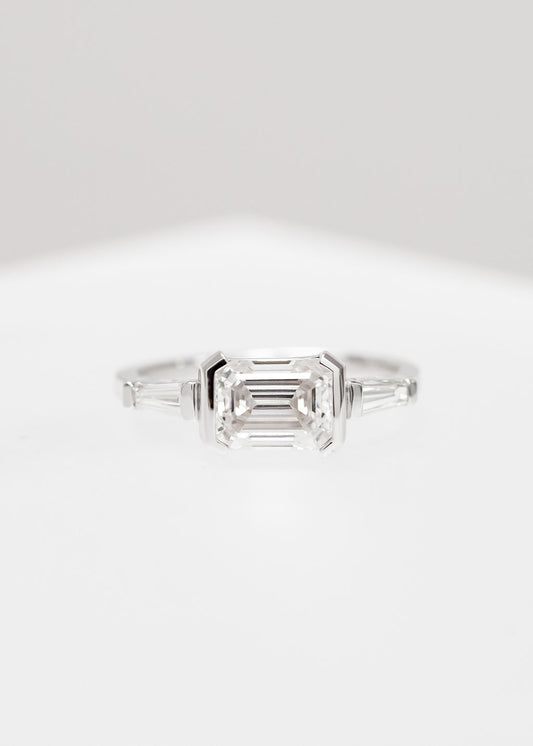 East west emerald cut moissanite three stone engagement ring in 14K white gold with half bezels and tapered baguette side stones