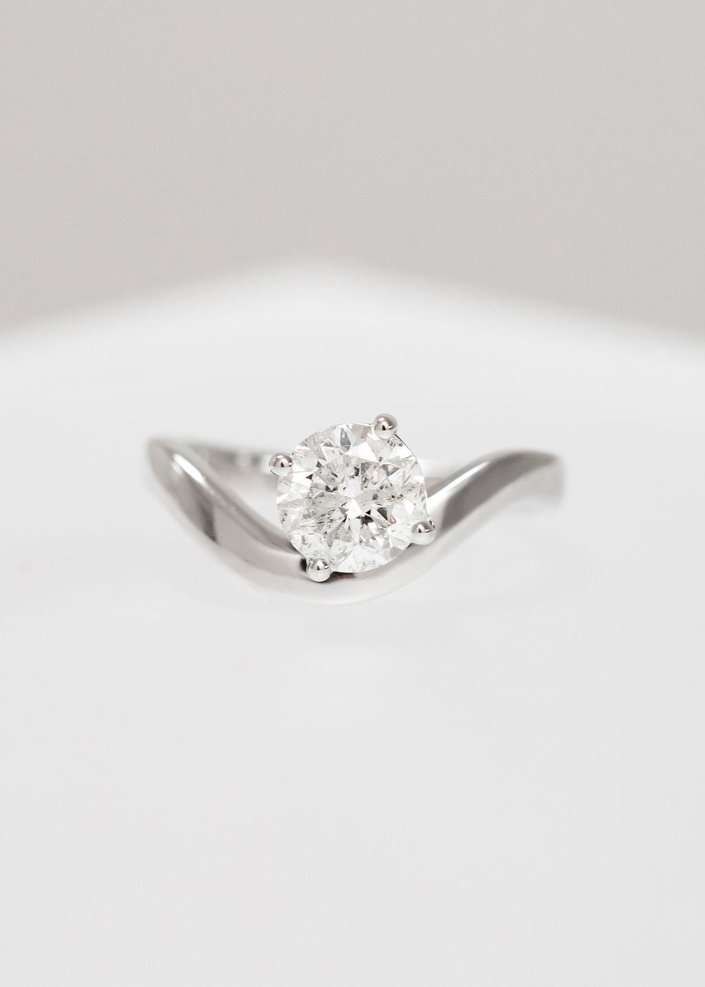 Asymmetrical round natural diamond solitaire engagement ring in 14K white gold with a modern curved band