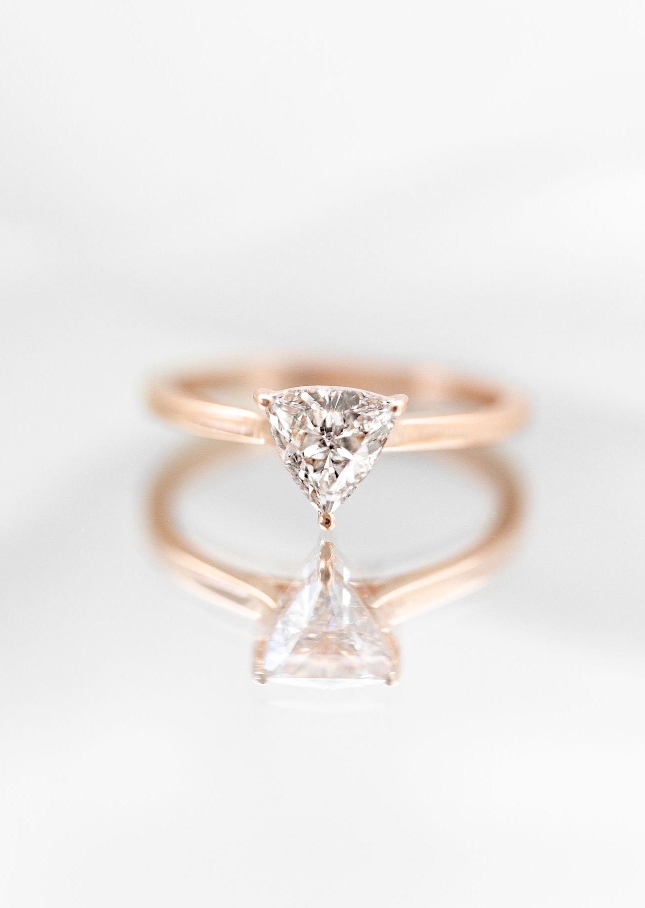 Stunning minimalist engagement ring featuring a unique trillion cut diamond, set in a sleek rose gold band. This asymmetrical engagement ring exemplifies modern elegance with its clean lines and a distinctively shaped diamond that captures light magnificently. Perfect for those seeking a contemporary, non-traditional engagement ring, the design highlights simplicity and sophistication, making it a top choice for fashion-forward couples.