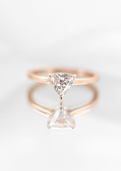 Stunning minimalist engagement ring featuring a unique trillion cut diamond, set in a sleek rose gold band. This asymmetrical engagement ring exemplifies modern elegance with its clean lines and a distinctively shaped diamond that captures light magnificently. Perfect for those seeking a contemporary, non-traditional engagement ring, the design highlights simplicity and sophistication, making it a top choice for fashion-forward couples.